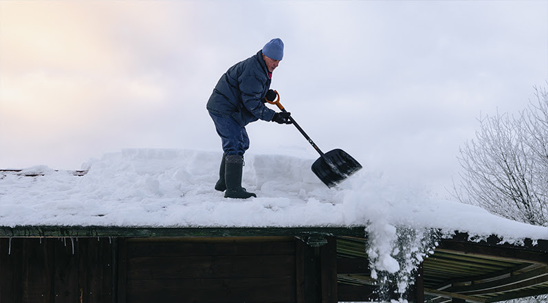 A Man Removing Snow From a Roof