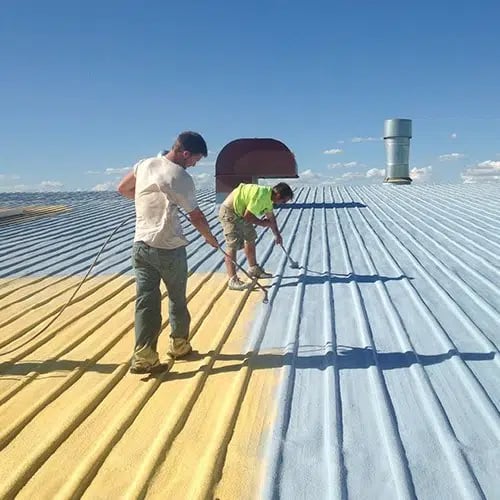 workers applying a roof coating on a metal roof