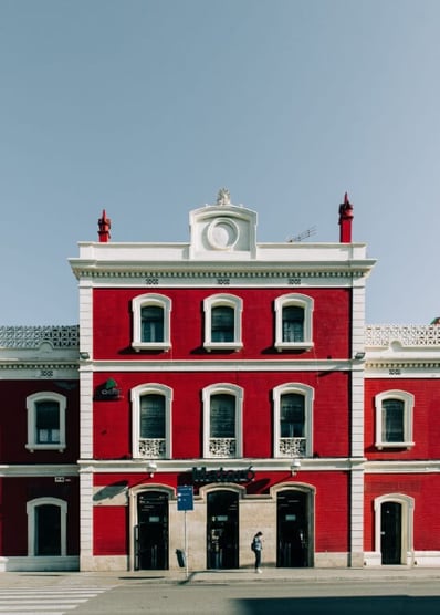 A bright red train station exterior, with white trim and a single person standing on the street outside.